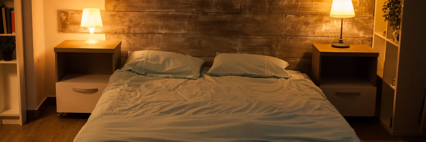 A made bed at night between two nightstands, each with a warm glowing bedside lamp.
