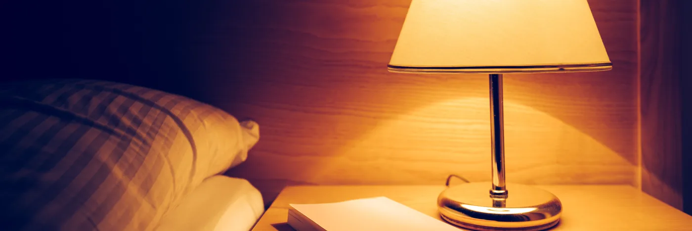 A warm bedside lamp lighting a pillow and an open book on a night table.