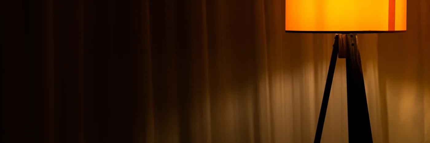 A simple floor lamp glowing warm orange in the corner of a darkened room.