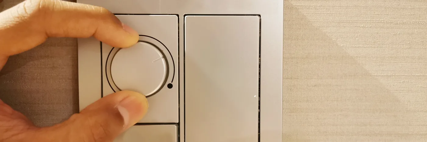 A hand turning the dial of a wall-mounted dimmer switch.