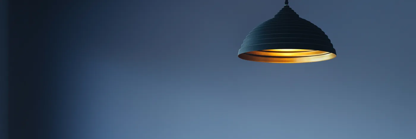 A single pendant lamp hanging against a deep blue wall, its shade glowing warm amber inside.