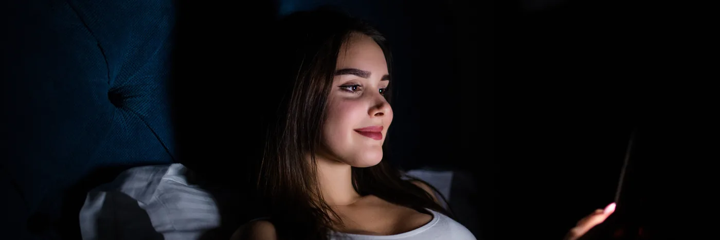 A face lit only by the blue-white glow of a phone screen in an otherwise dark bedroom.