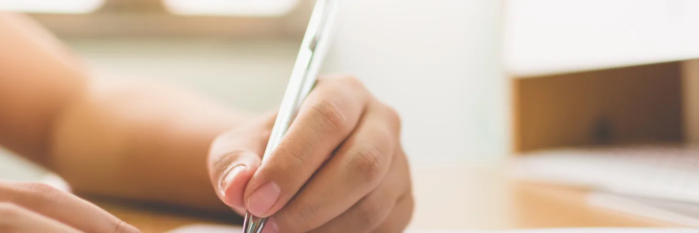 A hand signing a paper form with a pen on a desk.
